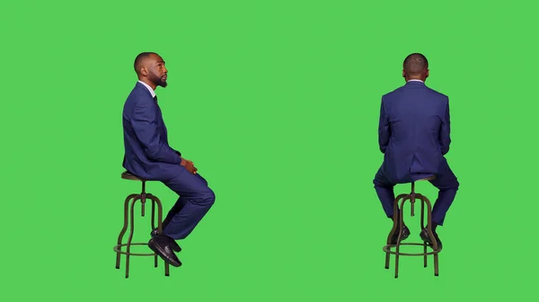 積極的な笑顔の人は 緑の画面上の椅子に座って 周りを見て 何かを待っている 男性起業家着用オフィススーツ以上フルボディグリーンスクリーン背景 — ストック写真