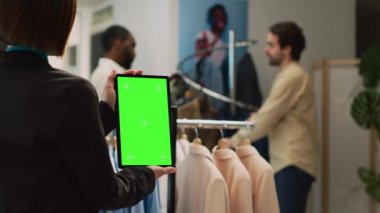 Asyalı genç işçi yeşil ekranlı tablet kullanıyor, mağazada çalışıyor. Krom anahtar ekranlı aygıt tutan kadın yardımcısı ve izole edilmiş model ekran, boş telif alanı.