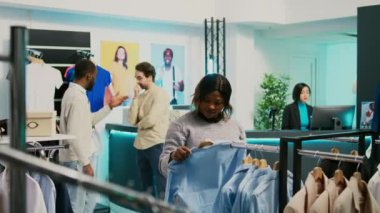 Afro-Amerikalı bir kız alışveriş merkezindeki çevrimiçi pazar hisselerini kontrol ediyor, akıllı telefonu yeni moda ürünlere bakmak için kullanıyor. Genç bayan alışverişçi yeni moda koleksiyonunu inceliyor, küçük iş konsepti.