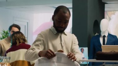 Afro-amerikalı bir adam mağazadaki raflardaki tişörtleri kontrol ediyor, alışveriş merkezinden mal almak istiyor. Şık bir yaşam tarzı olan erkek müşteri perakende piyasasını ziyaret ediyor..