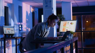 Corporate worker checking graphs on monitors planning financial investment to increase profit. Office employee analyzing economy diagrams on screen, working at night after hours. Handheld shot.