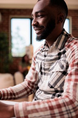 Kız arkadaşı kanepede kitap okurken Afrikalı Amerikalı bir adamın sosyal medya içeriğini bilgisayardan taramasının portresi. Uzaktan kumandalı çalışan Freelancer evdeki oturma odasında oturuyor.