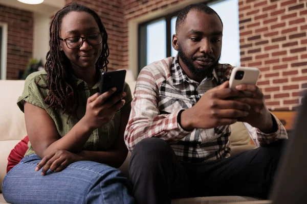 stock image African american couple spending time looking at social media content on smartphones and ignoring each other on couch. Man and woman living together upset after arguement using mobile phones.