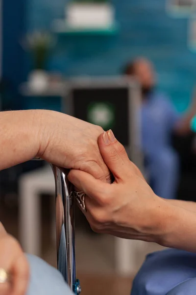 車椅子で高齢者の手を握っている医療助手は 診察前に神経を落ち着かせるのに役立ちます 高齢者のケアと治療に特化したセンターの専門看護師 — ストック写真