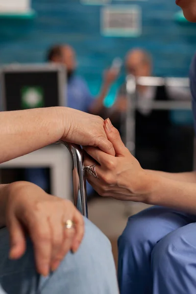 Nurse holding hand of an elderly patient in wheelchair, giving support and motivation in difficult moments. Professional nurses specialized in nursing home care for seniors.