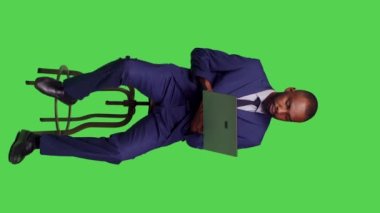 Dikey video: Şirketin internet sitesinde arama yapan, sandalyede oturan ve stüdyoda dizüstü bilgisayar kullanan çalışanlarının ön görüntüsü. Kablosuz bilgisayar üzerinde internet ağı sayfası ile çalışan yetişkin girişimci