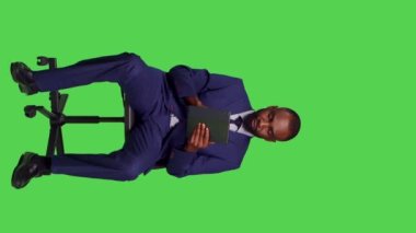 Dikey video: Afro-Amerikan bir adamın internet sitesine girip internet üzerinden dijital tablet ile ilgili iş bilgileri aramasının ön görüntüsü. Takım elbiseli genç işadamı oturuyor.
