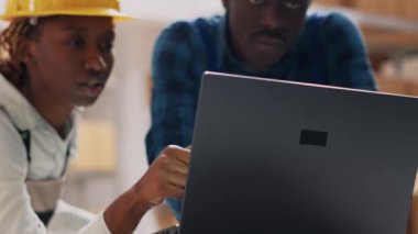 Depoda çalışan tulumlu iki genç laptodaki ürünleri okuyor. Mallara bakan bir grup işçi raflardaki kutulara, küçük işletmelere bakıyorlar. El kamerasıyla..