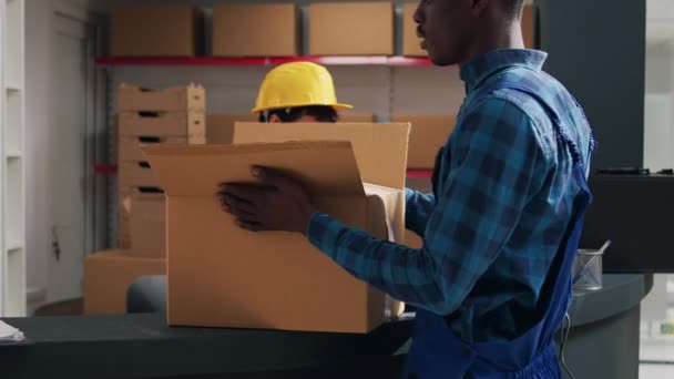 アフリカ系アメリカ人の男性は 出荷や流通のための注文を準備するために粘着テープを使用して 製品の箱を密封します 段ボールパックの倉庫商品を梱包する若い従業員 — ストック動画
