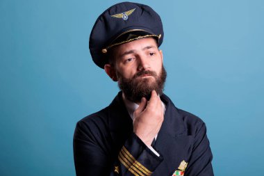 Üniformalı, düşünceli, kararsız havayolu pilotu. Düşünceli, dokunaklı, karar veren, fikir üreten. Şüpheli bir yüz ifadesi portresi olan dalgın bir uçak pilotu.