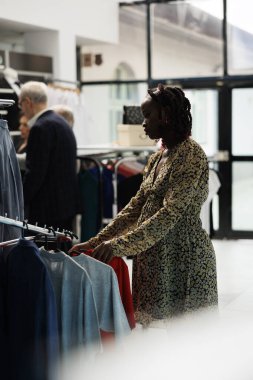 Hamile bir kadın elbise mağazasında son moda hamilelik kıyafetleri alıyor, tişörtleri kontrol ediyor. Afrikalı Amerikalı müşteri modern butikte annelik için moda ürünler alıyor.