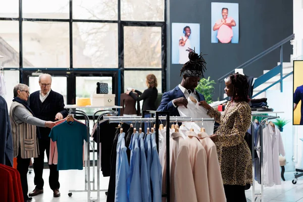 怀孕妇女帮助丈夫穿上正式的白衬衫 在购物中心查看材料 非洲裔美国人夫妇在现代精品店购买时尚服装和时髦商品 — 图库照片