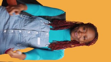 Dikey video: Afrikalı Amerikalı gezgin kameraya başparmak işareti yapıyor, stüdyoda başarı ve onayı ifade ediyor. Genç bir turist gibi görünüyor. Tatildeki olumlu kişi.