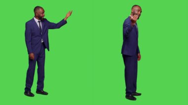 Şirket çalışanı birini çağırıp, el sallayarak ona eşlik etmesini istiyor. Erkek ofis çalışanı, yeşil perde arkasında resmi takım elbise giyiyor..