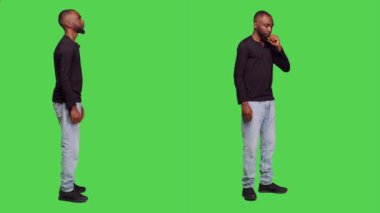 Afrikalı Amerikalı bir adam stüdyoda sabırsız bir şekilde bekliyor, kamerada bir şeyler düşünüyor. Erkek insan, sabırla beyin fırtınası yapıyor, tüm vücudun yeşil ekranının önünde duruyor..