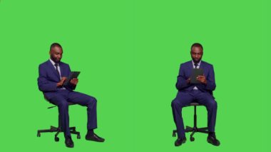 Afrikalı Amerikalı adam internet sitesini karıştırıyor, internet sayfalarında dijital tablet hakkında iş bilgileri arıyor. Takım elbiseli genç işadamı tüm yeşil ekranda oturuyor..