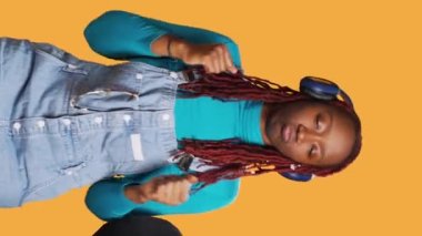 Dikey video: Afrikalı Amerikalı kız hava öpücüğü gönderiyor ve kulaklıkla müzik dinliyor, stüdyoda flört ediyor ve romantik davranıyor. Neşeli mutlu kadın dans ediyor ve neşeli hissediyor, romantizm işareti.
