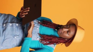 Dikey video: Afro-Amerikan kız web sitesini dizüstü bilgisayarla tarıyor, uçak uçuşu sırasında online web sayfası kullanıyor. Modern kadın turist sosyal medya uygulamalarını kontrol ediyor, el çantası ve bagaj taşıyor..