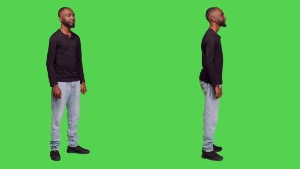 非裔美国人在演播室里微笑 摆出姿势 穿着衬衫和牛仔裤 全身上下都是绿色的背景 年轻人自信 随意的男性模特儿 — 图库视频影像
