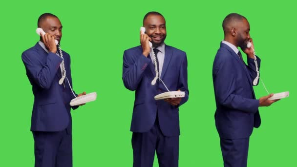 アフリカ系アメリカ人の男性は 固定電話を使ってマネージャーに電話をかけ スタジオでのリモートチャットのためのコードで事務所の電話に応答する 緑の画面の背景 ビジネススーツを身に着けている男性従業員 — ストック動画