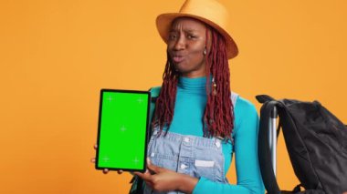 Stüdyoda tablet tutan neşeli bir kadın izole edilmiş yeşil ekran şablonuyla çalışıyor. Boş krom anahtar ekranlı dijital aygıt gösteren kadın turist, ekranda telif alanı.