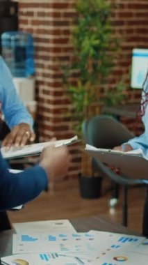 Dikey video: Yönetim kurulu toplantısında belgeleri inceleyen şirket çalışanları, tabletle yıllık veri sunumu üzerinde çalışıyorlar. Meslektaşlar iş uzmanlığı planıyla karı artırmaya çalışıyor.