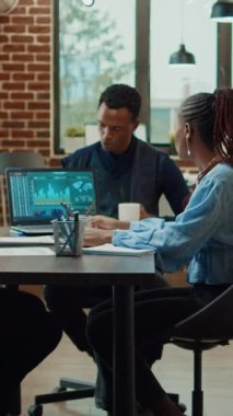 Dikey video: Dizüstü bilgisayar ve dosya raporlarındaki çevrimiçi veri analizlerine bakarak sunum üzerinde çalışan başlangıç grubu. Proje bilgisi ve araştırması ile yeni bir vizyon yaratmak için takım çalışması yapan çalışanlar