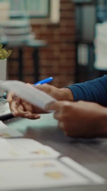 Dikey video: Şirket asistanı yeni araştırma planı oluşturmak için dosyalar, iş belgeleri ve istatistikleri gözden geçiriyor. Çalışma alanında yıllık raporları inceleyen genç bir adam