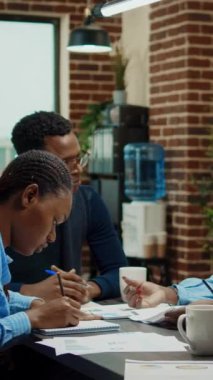 Dikey video: Şirket çalışanları toplantı ofisindeki belgeleri inceliyor, şirket bilgileriyle belgeleri inceliyor. Birlikte çalışma alanında yeni şirket vizyonu üzerinde çalışan Afrikalı Amerikalılar.