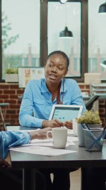 Dikey video: Araştırma planını gösteren bayan yönetici, yönetim kurulunda tabletle birlikte sunum yapıyor. İş arkadaşlarıyla iş geliştirme sonuçlarıyla yeni stratejiyi tartışıyor.