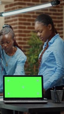 Dikey video: Ofisteki yıllık veri istatistiklerini incelemek için boş model görüntüleme kullanarak, yeşil ekranlı dizüstü bilgisayara sahip işçiler. Meslektaşlar raporları kontrol ediyor, izole edilmiş krom anahtar ekranla çalışıyor