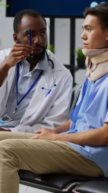 Dikey video: Doktor, hastane bekleme alanındaki check-up muayenesi sırasında hastanın göz vizyonunu inceleyerek sağlık hizmetleri tedavisini açıkladı. Asyalı adam boyun üstüne boyun tasması takıyor.