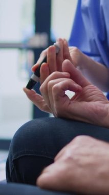 Dikey video: Diyabet hastası kıdemli hastalarda muayene sırasında tıbbi glukometre kullanarak kan örneğinde insülin seviyesini ve glikozu ölçen asistan. Hastanede tıbbi test yapan Asyalı hemşire.