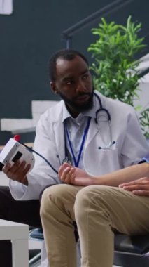 Dikey video: Travmatolog Asyalı hastada hipertansiyon ve hipotansiyon ölçüyor, yüksek veya düşük nabız basıncını ölçmek için tıbbi tonometre kullanıyor. Doktor enstrüman ile genç yetişkinlere danışmak