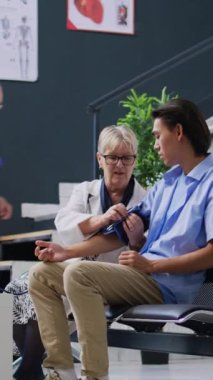 Dikey video: Hasta hipertansiyonu ve tansiyonunu ölçmek için tonometreyle kardiyoloji muayenesi yapan yaşlı doktor, kan basıncını aletle ölçüyor. Asyalıları ölçen bir doktor.