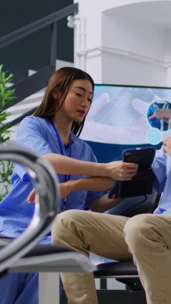 垂直ビデオ 病院の待合室での検査訪問中に 患者の高血圧と血圧を測定し 計測器で心臓検査を行うためのアシスタント アジア人男性を調べる看護師 — ストック動画