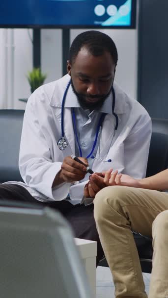 垂直ビデオ 医師は病院の待合室で診察予約時にアジア人男性の血液サンプルをチェックし インスリンとブドウ糖のレベルを測定するために医療用血糖計を使用しています 医療支援 — ストック動画