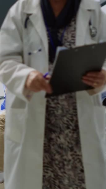 垂直ビデオ 負傷した患者の目のビジョンを検討看護師 病院の待合室で任命中に医療専門知識を議論 首の怪我の後に子宮頸部の襟を身に着けているアジア人男性 — ストック動画