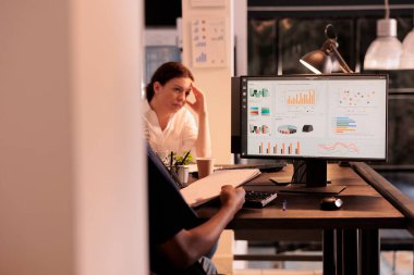 Ofis çalışanı bilgisayardaki analitik raporları analiz ediyor, panodaki çizelgeleri karşılaştırıyor, şirket araştırma sonuçları analizi yapıyor. Afrika kökenli Amerikalı iş adamı ofiste istatistikleri kontrol ediyor