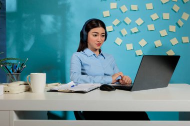 Şirket çalışanı, şirketin profesyonel çalışma alanında dizüstü bilgisayarının önünde oturmuş, ekrandaki e-postalara bakıyor. Çalışırken kablosuz kulaklık kullanan kadın.