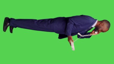 Dikey video: Sabit telefonlara cevap veren kendine güvenen bir çalışanın profili, stüdyodaki kabloyla ofis telefonunda uzaktan konuşma. Erkek müdür telefonda konuşuyor, tüm vücudu yeşil.