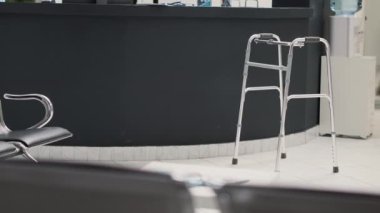 Lobide yürüyüş çerçevesi olan klinik bekleme salonu, bekleme odasında tıbbi raporları ve sandalyeleri olan boş resepsiyon masası. Hastahane koridorunda fiziksel bozukluklara yardım için.