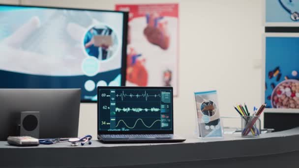 机の上のノートパソコン上で心臓病の診断 空の医療施設待機エリアでの心拍数と心拍数を示します ロビーに表示される心電図解析と心拍数の圧力 — ストック動画