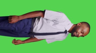 Dikey video: Kurumsal ofis işi için resmi takım elbise giymiş, yeşil perde arkaplanının üzerinde duran Afro-Amerikan bir adamın yan görüntüsü. Erkek çalışan işadamı şık ve pozitif hissediyor, yeşil ekran