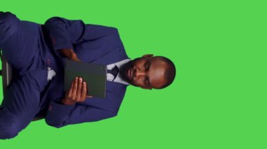 Dikey video: Stüdyoda sandalyede oturan dijital tablet kullanarak sosyal medya sayfasında kayan erkek girişimcinin ön görüntüsü. Modern aygıtlarda online ağ taraması yapan genç girişimci