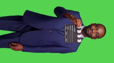 Dikey video: Genç yetişkin film yapımcısının prodüksiyon sonrası endüstrisinde flapperboard kullanarak stüdyoda film tahtasını çevirmesinin ön görüntüsü. İyimser iş adamı film yapımcılığı, takım elbise üzerinde çalışıyor.