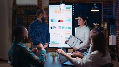 Diverse coworkers presenting company annual statistics report, employee planning marketing strategy in coworking space. Office workers in business meeting, revenue data presentation