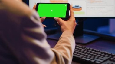 Yatay yeşil ekranlı akıllı telefonla çalışan girişimci, iş ofisindeki izole görüntüyü kullanıyor. Kadın yönetici telefondaki boş telif alanı ile krom anahtar şablonunu analiz ediyor.