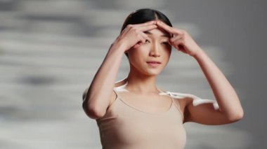 Yüzüne nemlendirici krem sürerek cilt rutini oluşturan Asyalı kadın, kamerada güzellik kozmetiği reklamı yapıyor. Özgüveni, vücut bakımını, kusurları teşvik eden genç doğal bir model..
