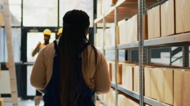 Depoda dijital tablet ve tarayıcıyla çalışan, barkodları erzak paketlerinde tarayan genç bir işçi. Erkek işçi depoda karton paketler için kalite kontrol yapıyor. El kamerasıyla..